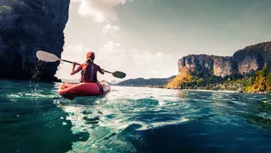 Red kayak on choppy turquoise water, flanked by tree-covered cliffs.
