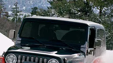 Red and black Jeep with a front winch, kicking up snow in a snowy landscape.