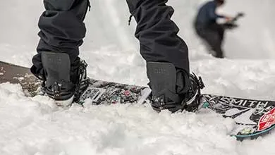 Close-up of snowboarder's boots in bindings on a snowy snowboard.