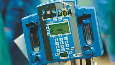 A blue medical infusion pump, close-up. It has a central digital screen with green text, a numeric keypad, and a top display showing '500'.