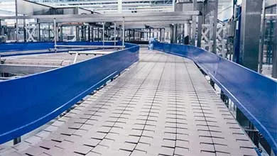 Empty industrial conveyor belt, white interlocking surface, blue side rails, curving through a facility.