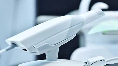 White handheld dental intraoral scanner on its stand.