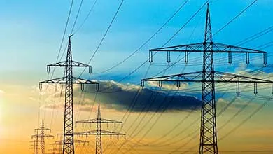 Silhouetted electricity pylons and power lines against a blue and golden sunset sky.