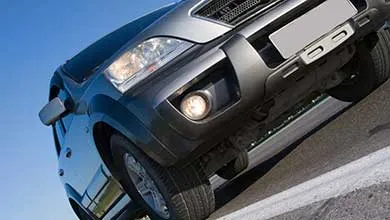 Low-angle view of a silver SUV driving up a steep hill under a clear blue sky.