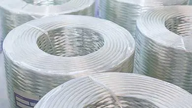 Multiple rolls of translucent, braided composite tubing tightly coiled and stacked in an industrial setting.