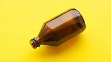 A brown glass bottle lies on its side against a solid yellow background.