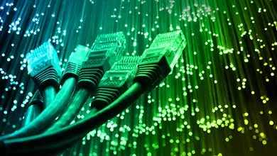 Close-up of Ethernet cable connectors in front of glowing blue and green fiber optic strands.