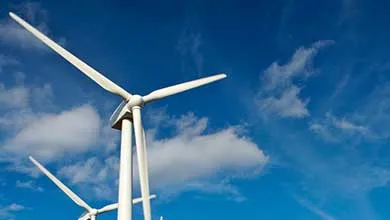 Wind turbines standing across an open landscape under a bright blue sky with scattered clouds.