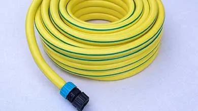 Coiled yellow garden hose with green stripes and a blue-and-black connector, on a plain light background.